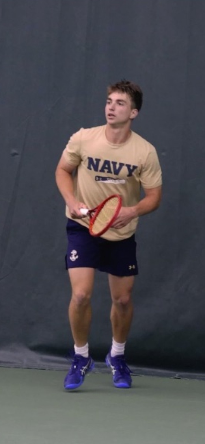 Jake Fishkin holding a tennis racquet on court in Navy tennis apparel